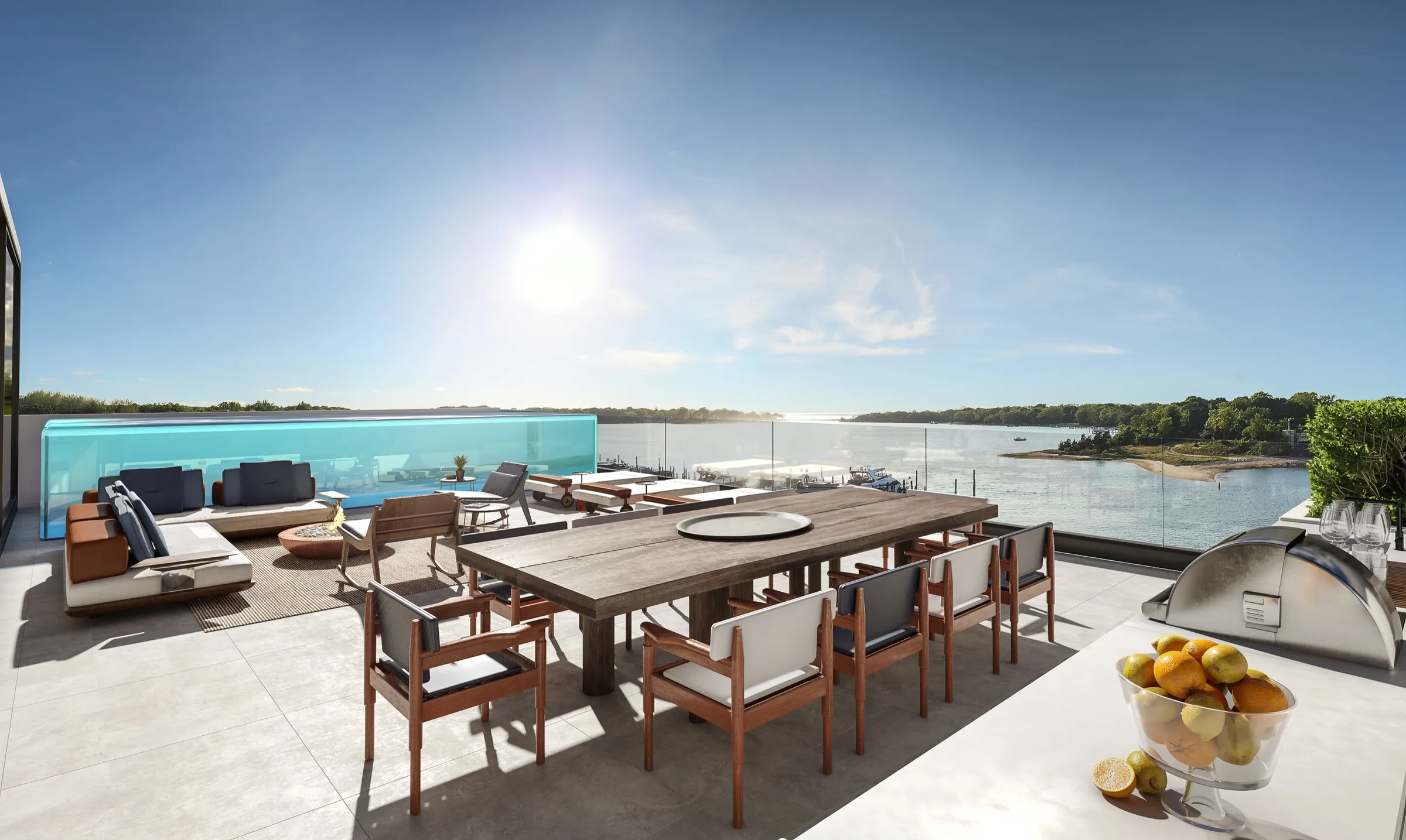 3D rendering of the rooftop deck of Residence B at 2 West Water Street, an outdoor dining table and kitchen beside a glass-walled plunge pool and lounge, with Sag Harbor Cove and its far shore beyond.