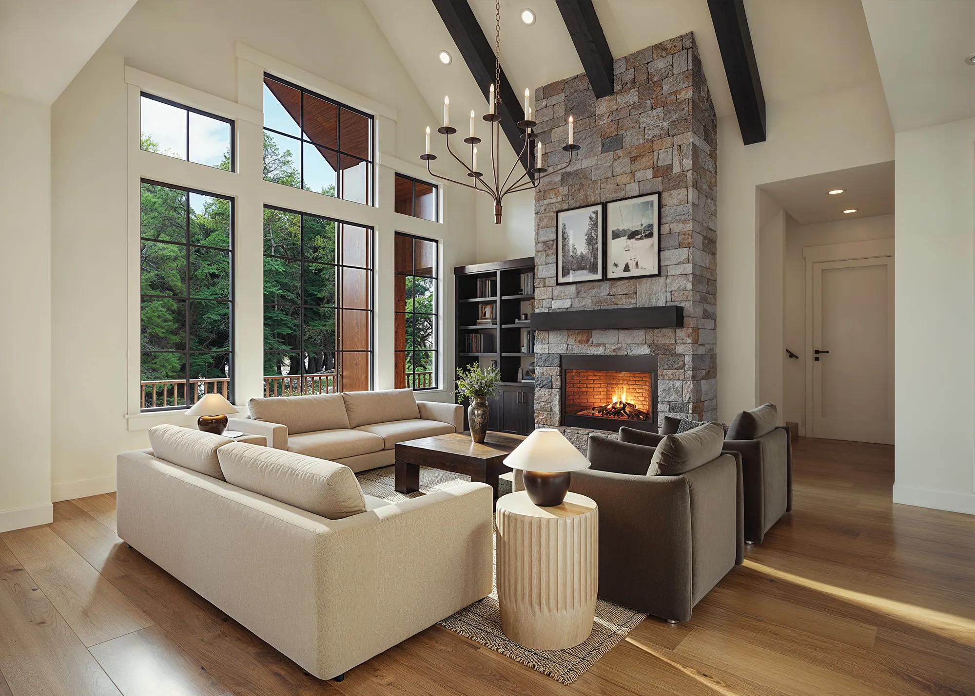 Photorealistic 3D rendering of the great room of the Haystack model by Alturas Homes, focused on the floor-to-ceiling stone fireplace flanked by tall windows, with neutral sofas and lounge chairs on a wood floor.