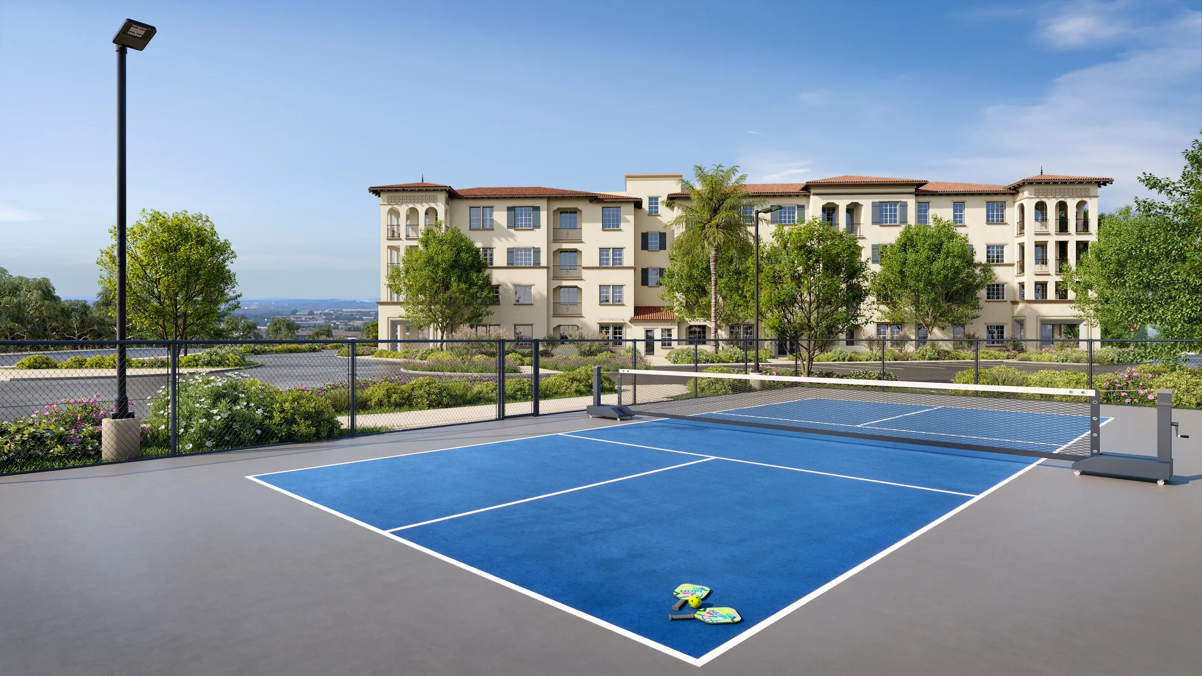 Daytime 3D rendering of the pickleball court at Anindell in Folsom, California, a fenced blue-and-grey court with paddles and a ball on the surface, the cream-stucco Mediterranean buildings rising behind under a clear sky.