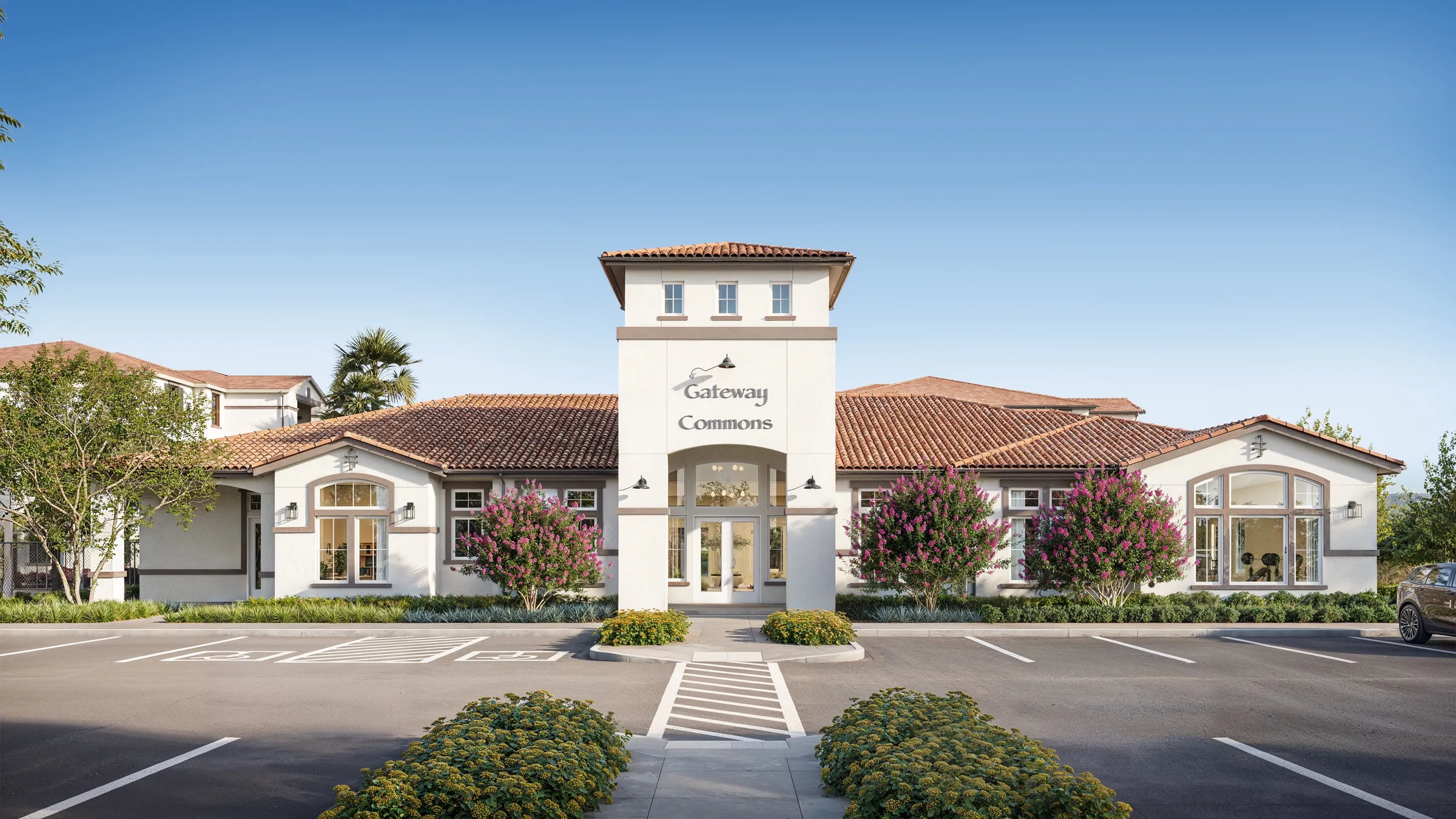 Front elevation of the Gateway Commons community building, a Spanish-Mediterranean leasing center with a central tower, arched entry, and crepe myrtles in bloom along the facade, a photorealistic 3D rendering.