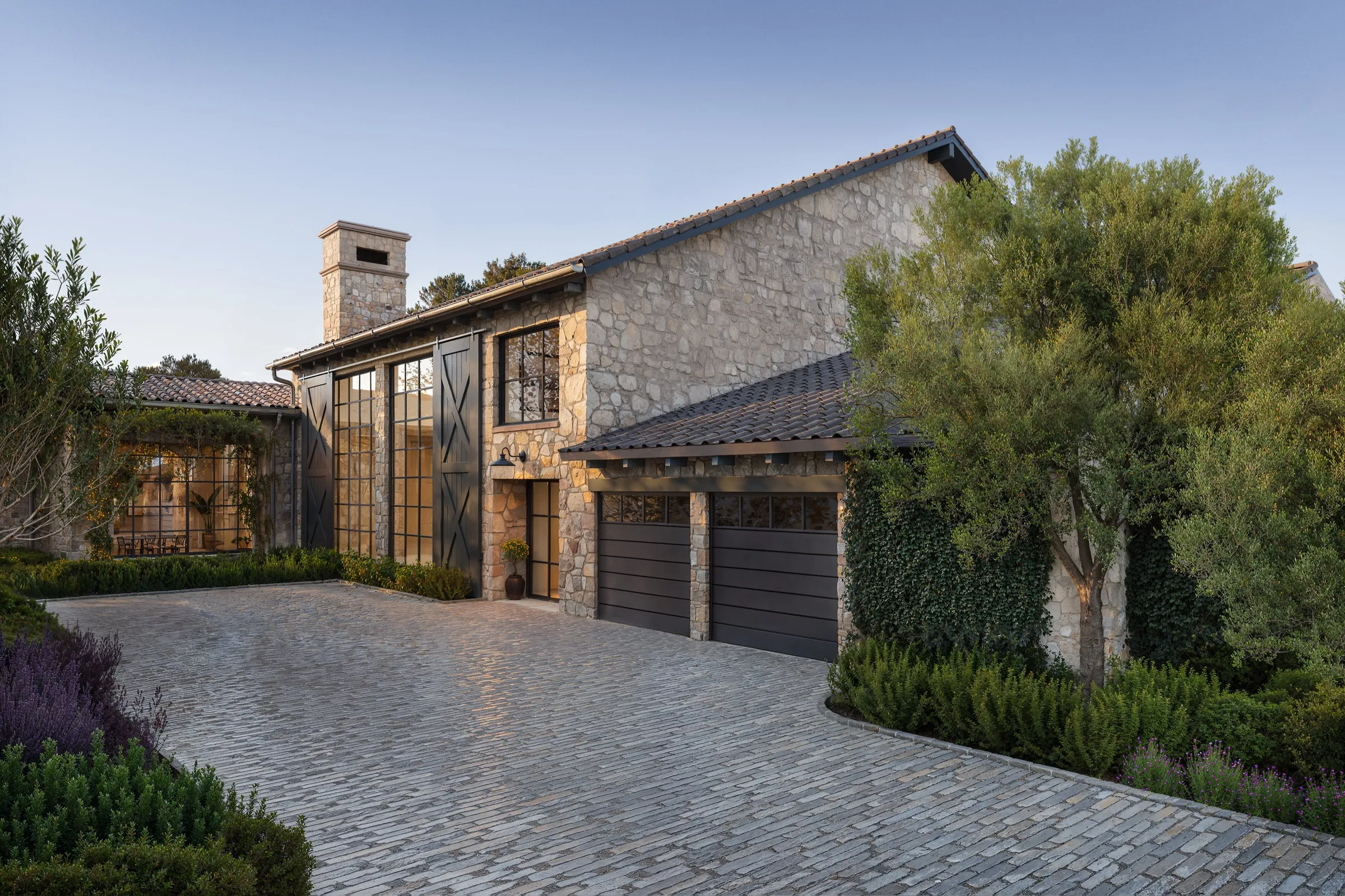 Exterior 3D rendering of a stone wine-country home with tall steel windows, a clay tile roof and a paver motor court among olive trees