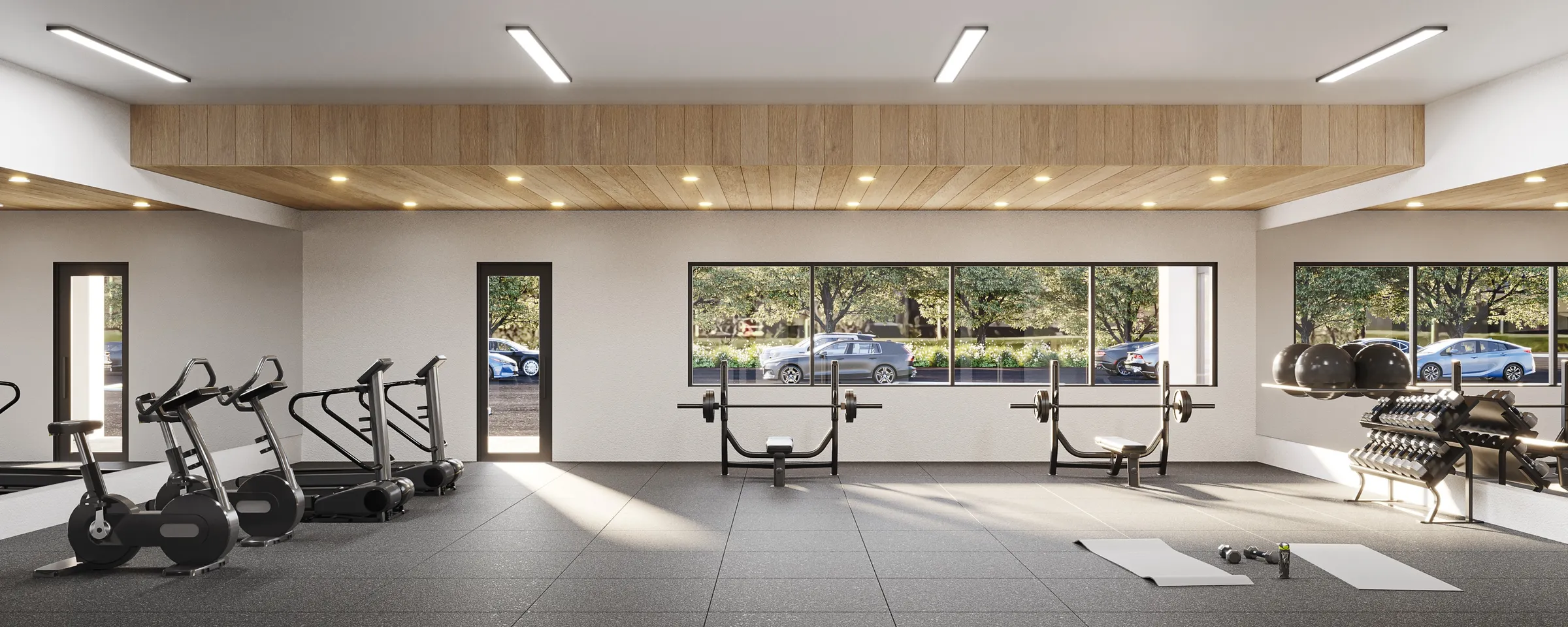 3D rendering of The Ivy’s tenant fitness center, with cardio machines, free weights, benches, and a yoga mat, lit by a row of windows onto a tree-lined parking lot.