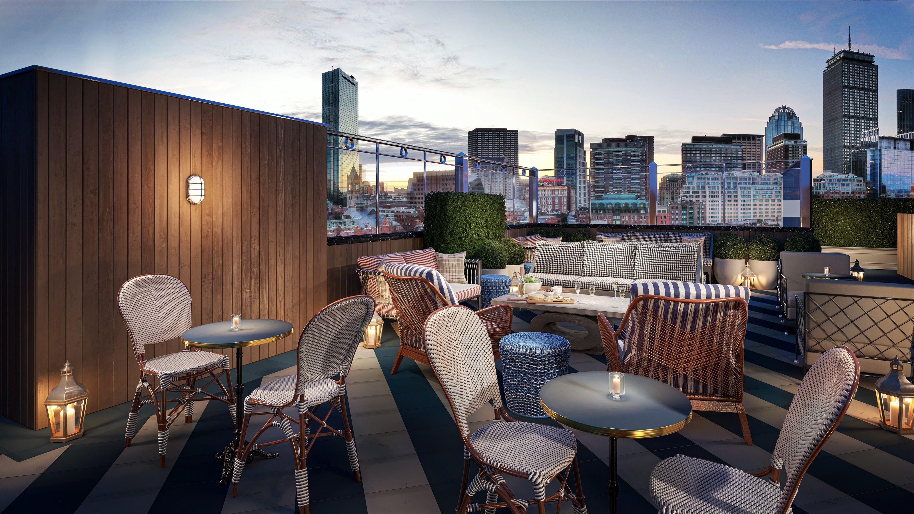 Interior 3D rendering of the roof deck at The 'Quin House at dusk, with bistro chairs and tables, a built-in sofa, lanterns, and clipped hedges framing the Back Bay and Boston skyline, the Prudential and Hancock towers visible.