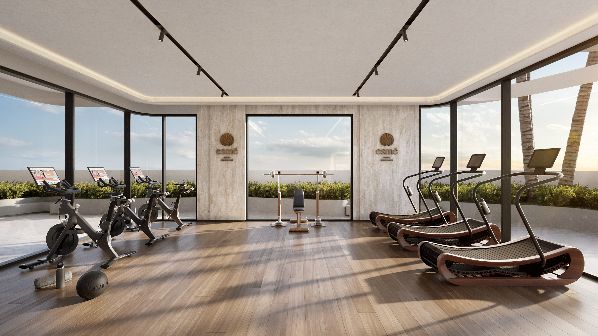 Interior 3D rendering of the fitness studio at Esmé Beach Residences, wood-floored with curved treadmills and spin bikes at panoramic windows, the project's brand mark on travertine walls, and palms outside the glass.